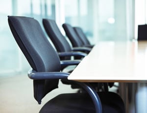Four empty office chairs line up at a boardroom table